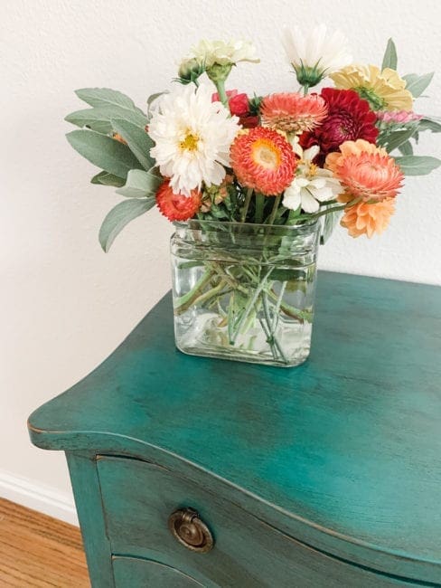 flowers on top of a small night stand painted with teal clay furniture paint and then distressed with black furniture wax